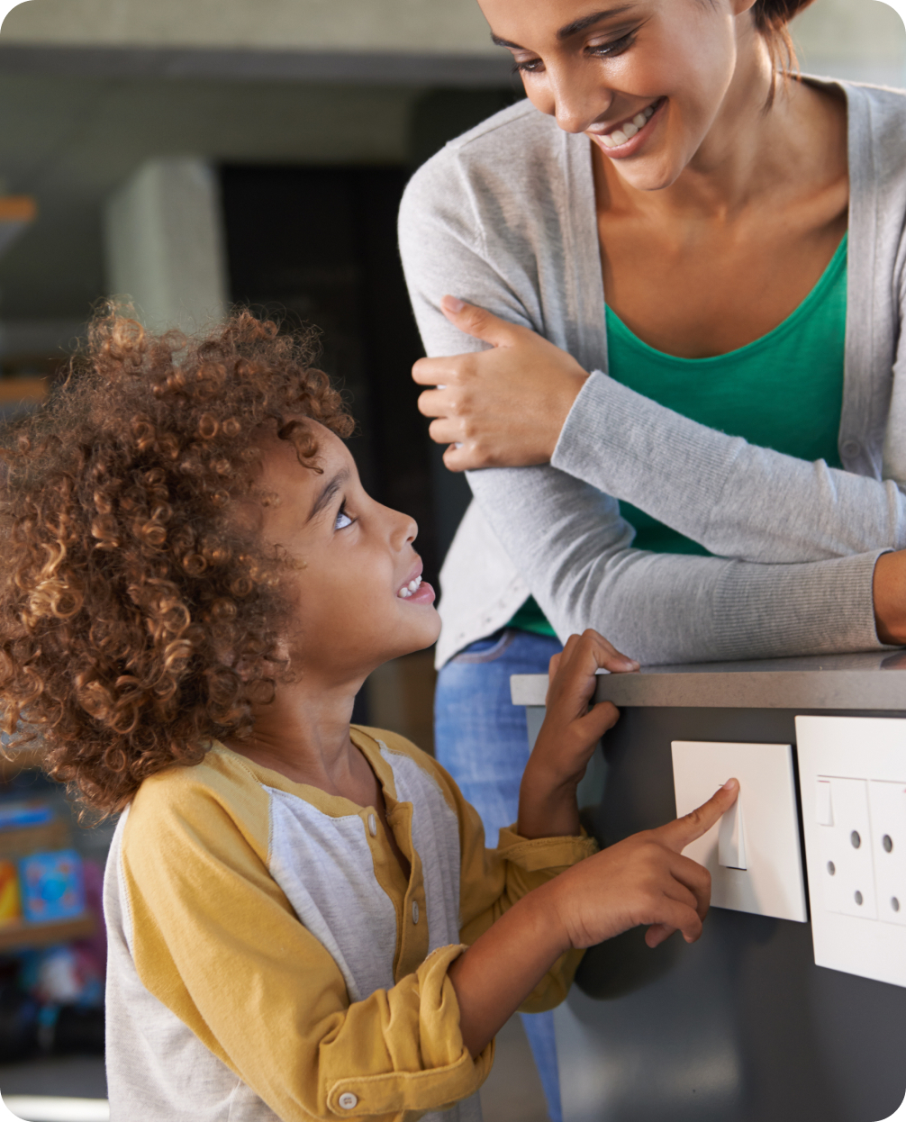 Mother smiling while looking at child that is smiling while touching a light switch.