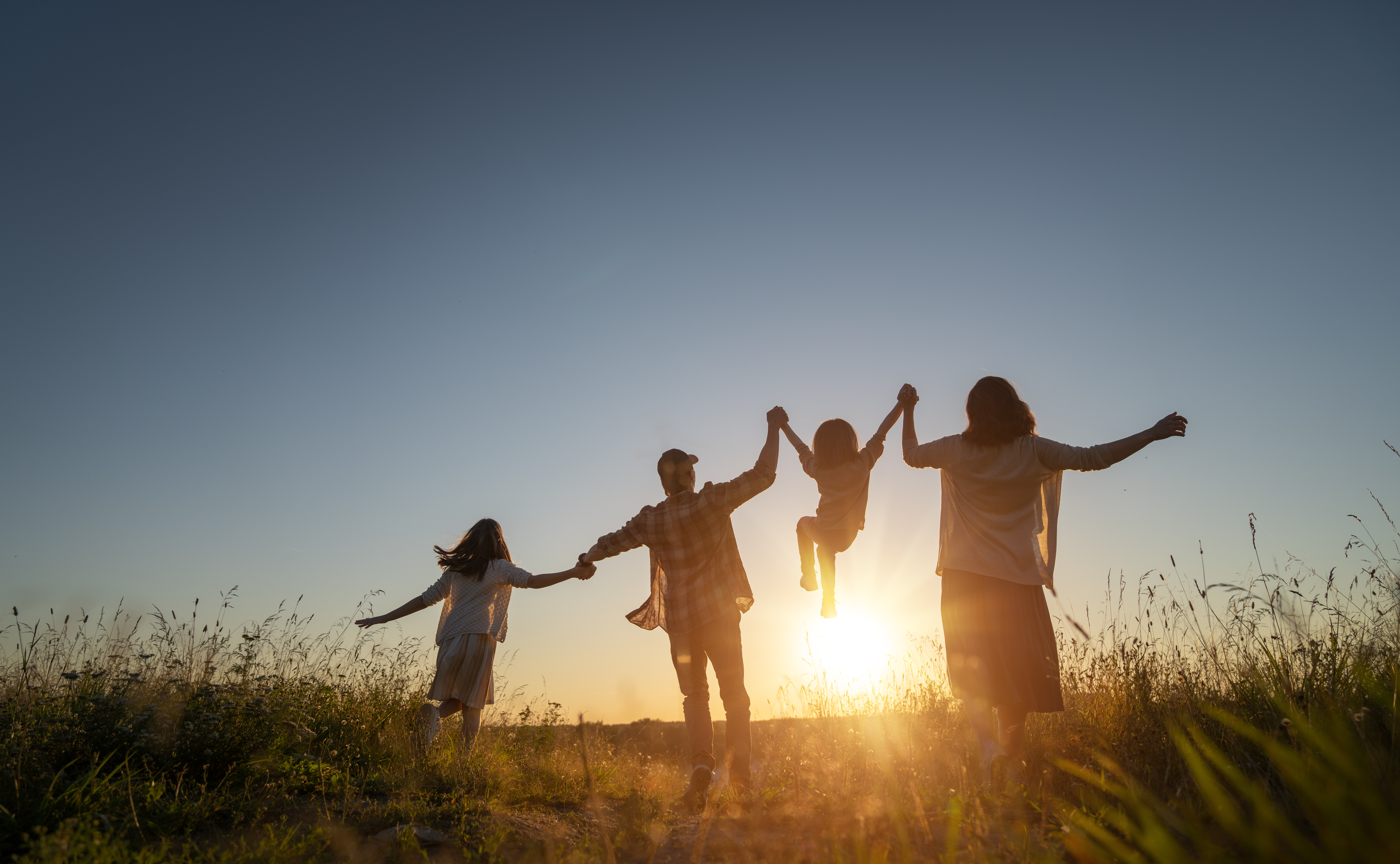 A family of 4 in a field with a sunrise. Community Solar helps them save money for what matters