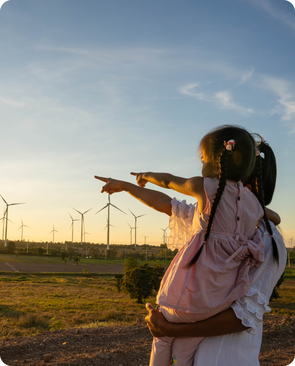 Mother and child pointing at a wind farm with a sunset and blue sky in the background.