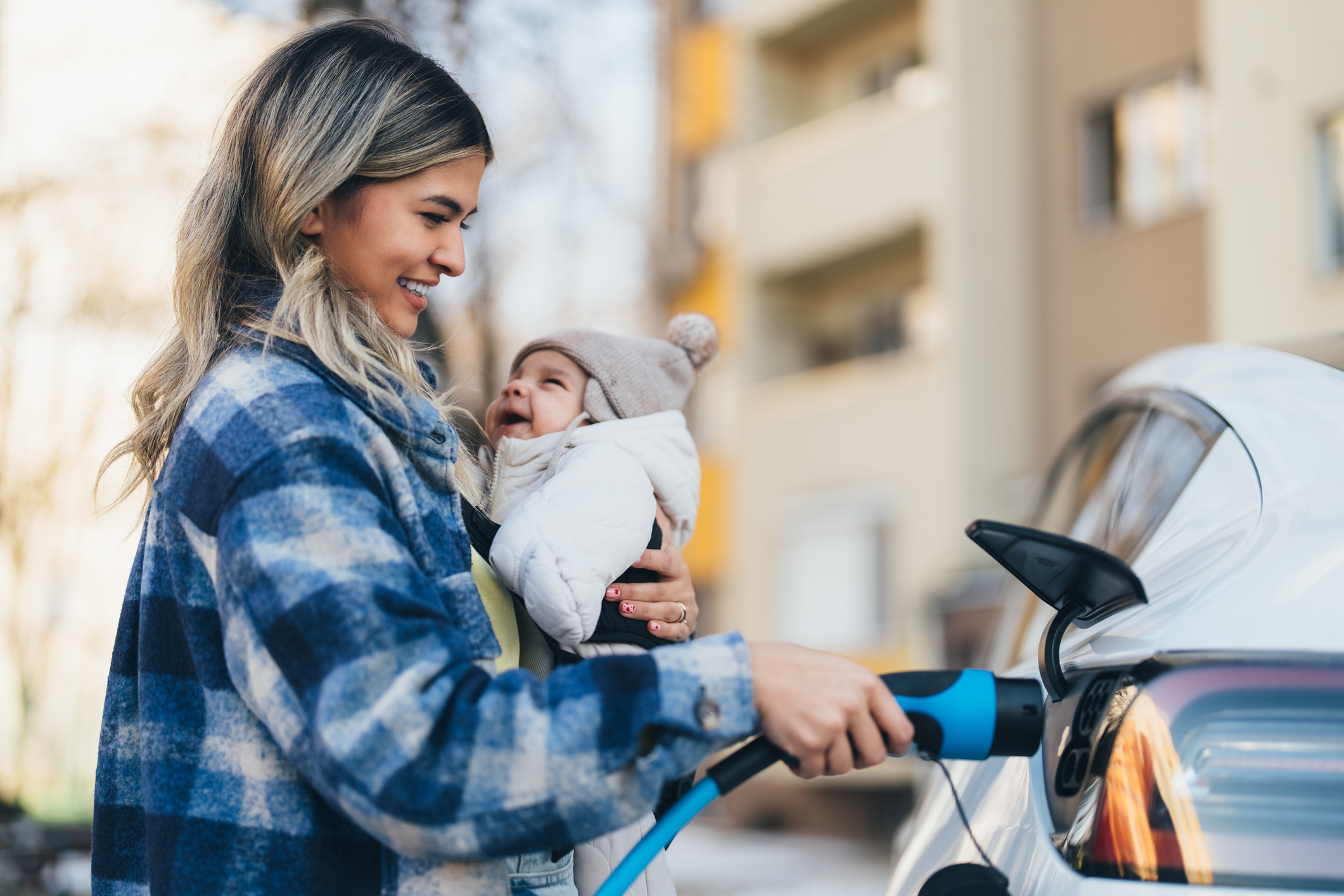 Mother charging her plug-in hybrid electric vehicle with her baby