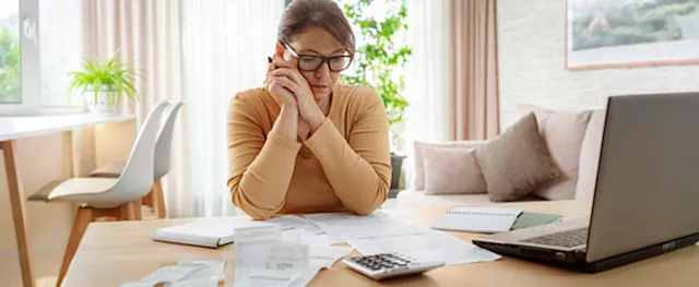 A woman reviewing bills and calculating payments to decide which debt to pay off first.