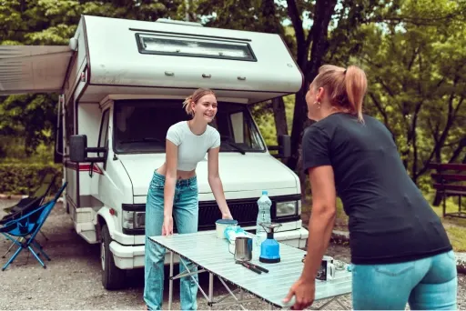 'Two women smiling and enjoying themselves while setting up camp around their RV