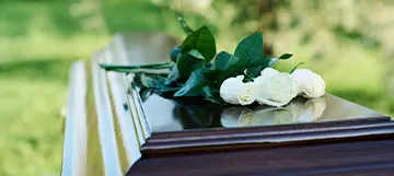 A casket with white roses on top in an outdoor setting.