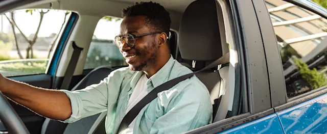 A man wearing a seat belt while driving a car on a sunny day.