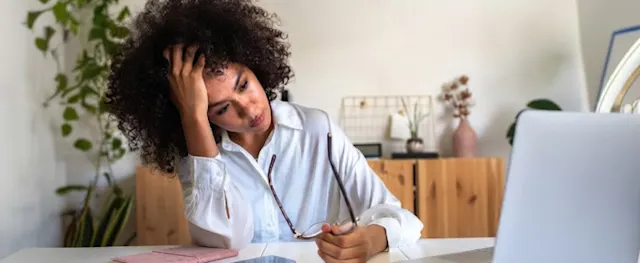 A woman looking stressed while working at her desk on a laptop, illustrating the challenges of zombie debt.