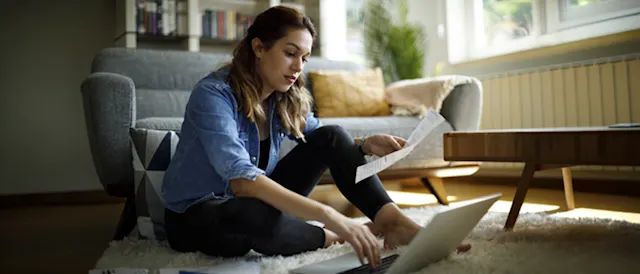 Woman reviewing financial documents on a laptop at home.