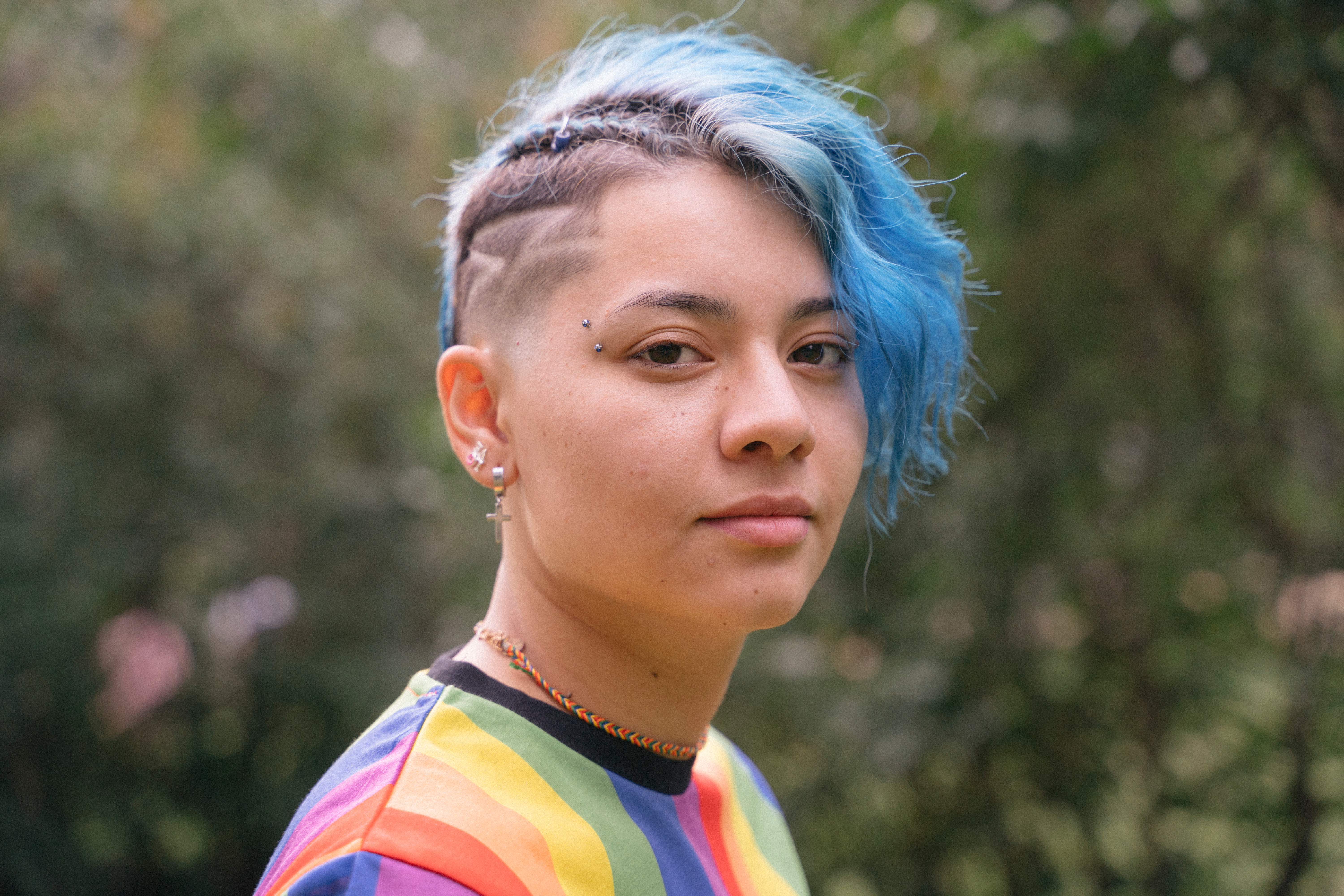 Woman with blue hair wand eyebrow piercing wearing rainbow t-shirt looking at camera