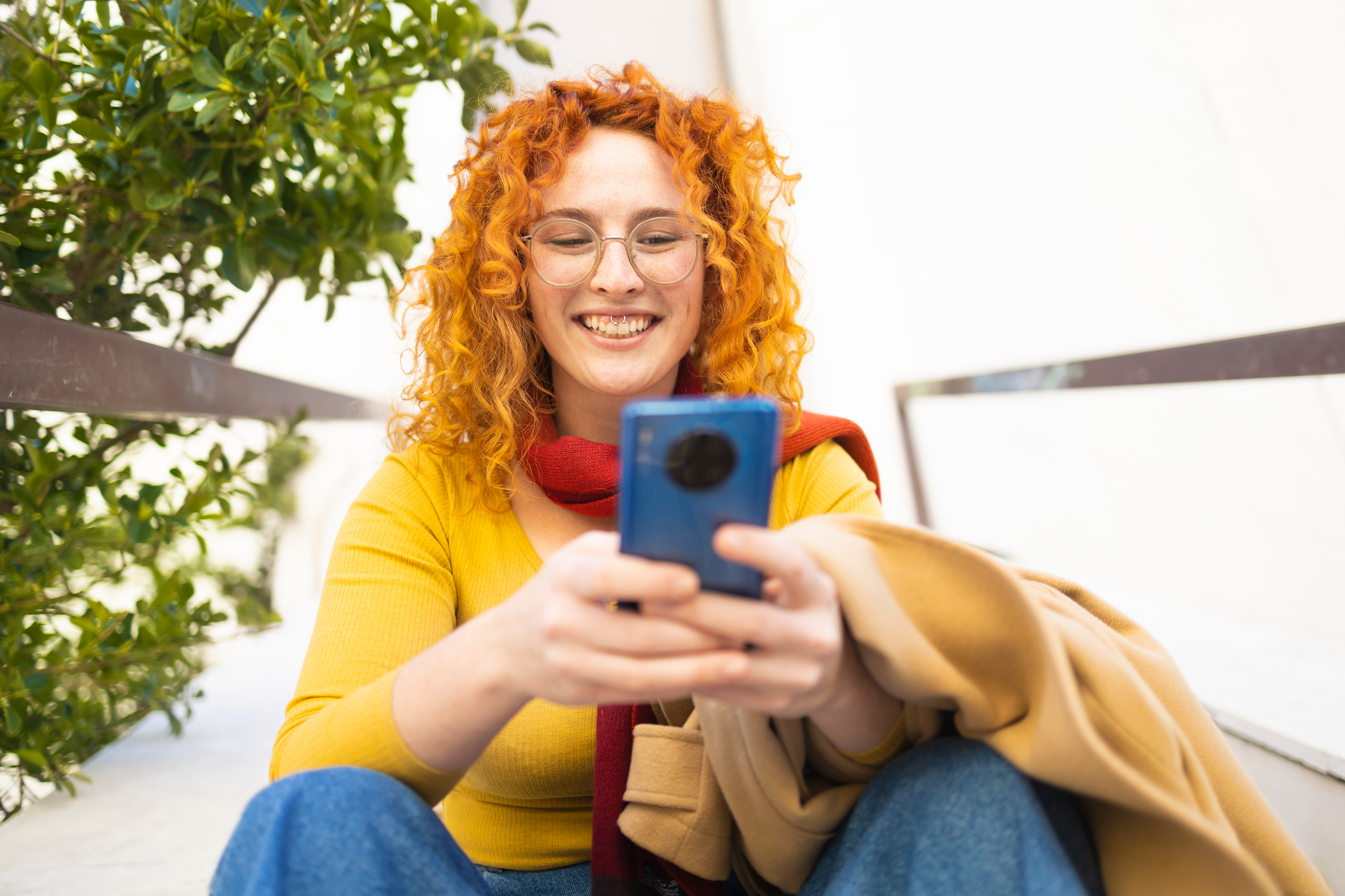Ginger woman in yellow using her smartphone