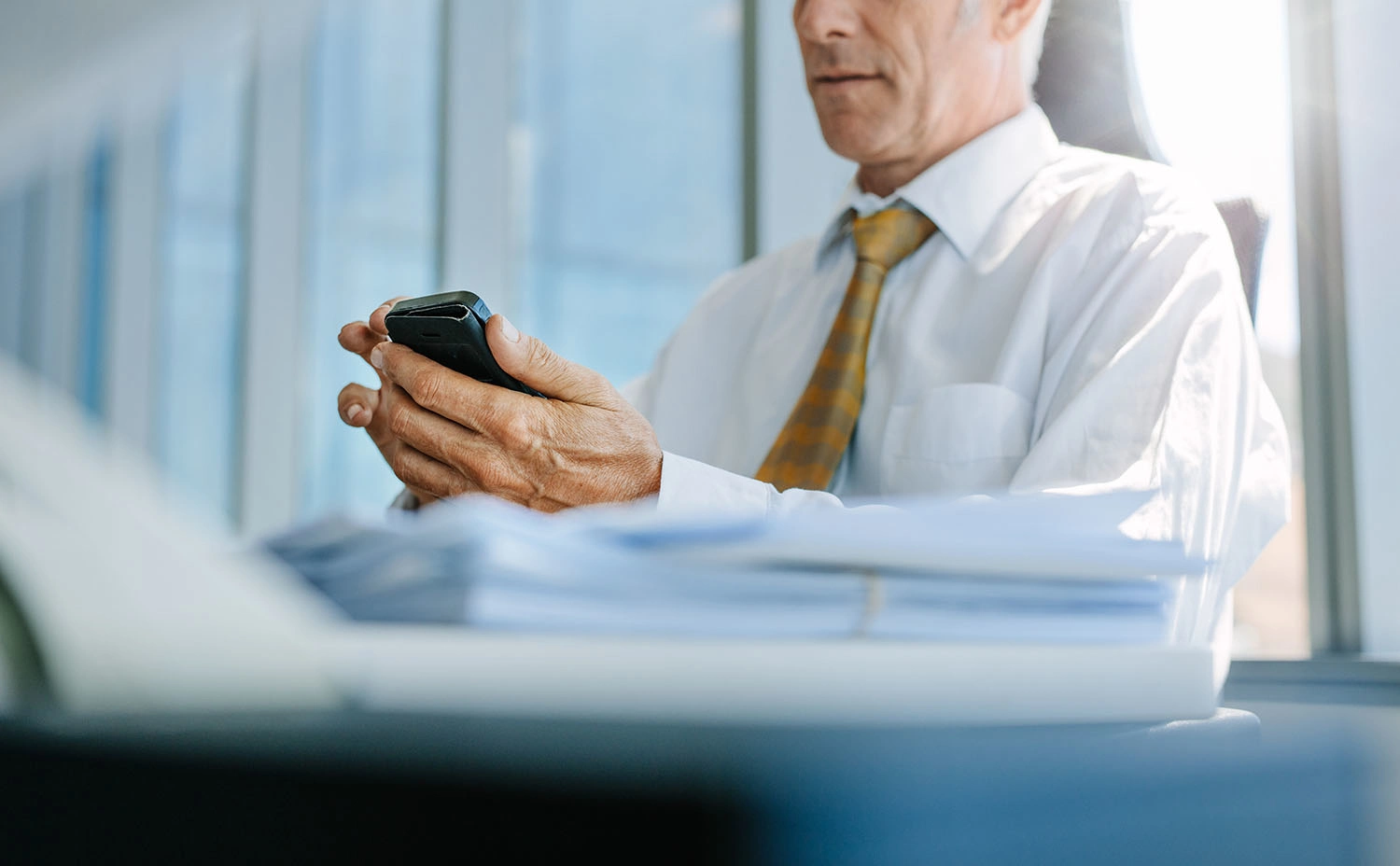 Ein älterer Geschäftsmann benutzt ein Mobiltelefon im Büro - 3:2