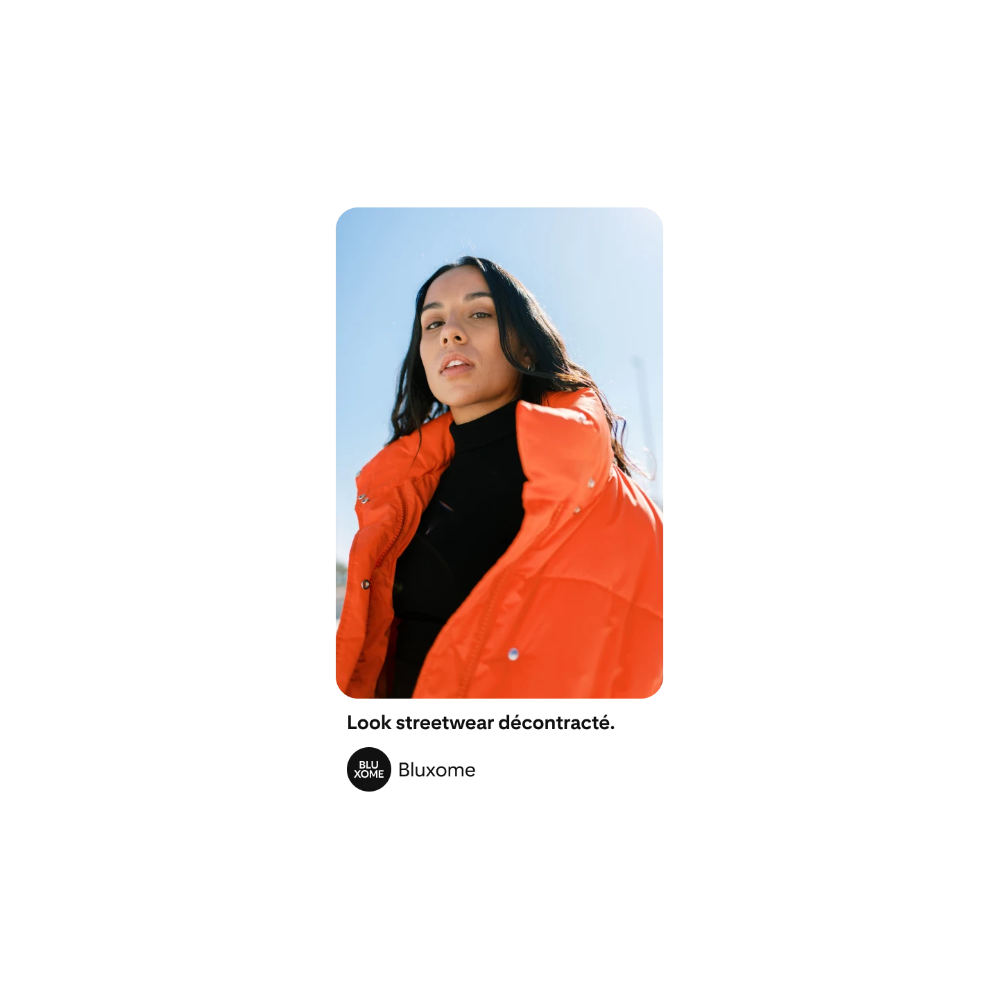 Une femme aux longs cheveux bruns prenant la pose devant l’appareil photo, habillée d’une doudoune orange et d’un col roulé noir.