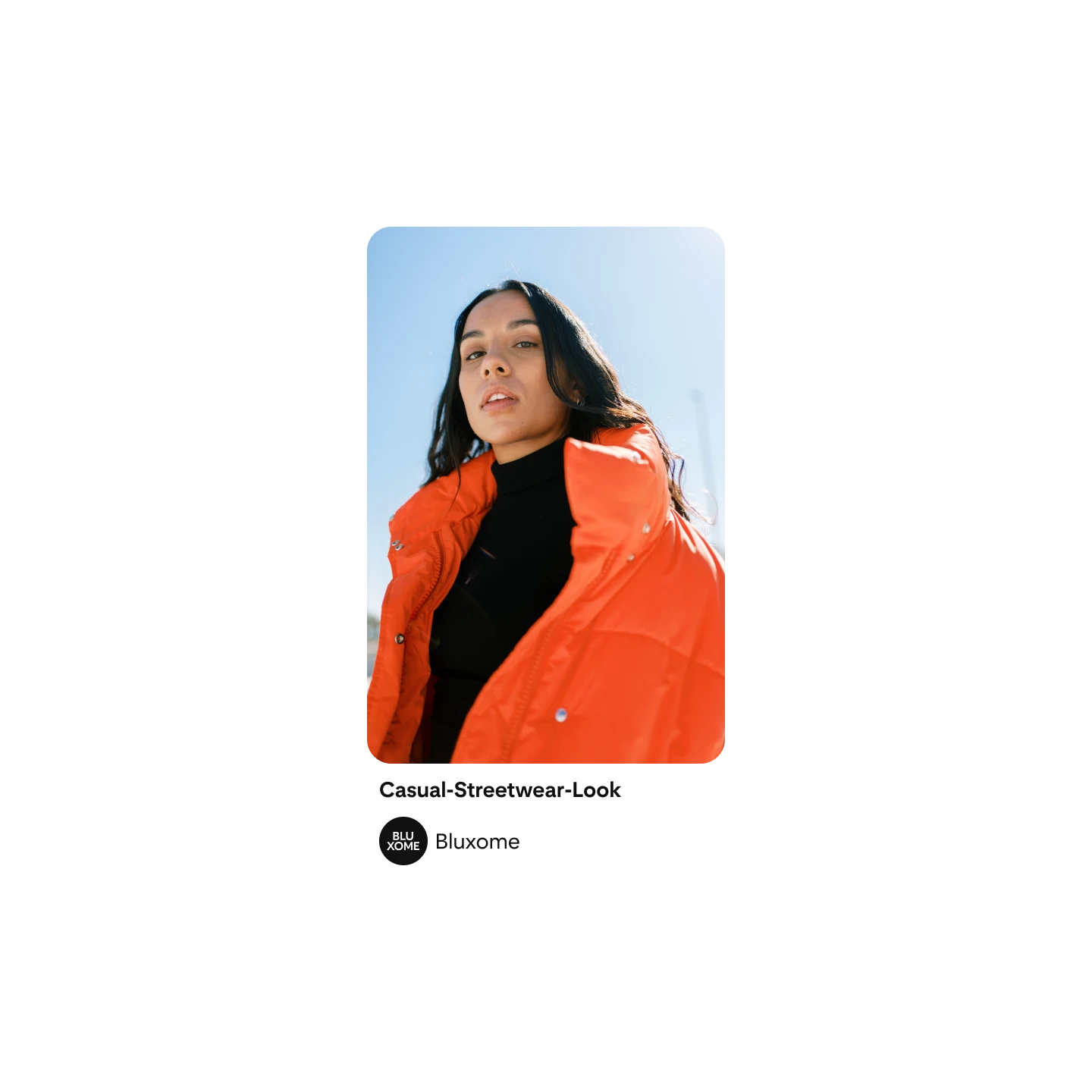 Eine Frau mit langen dunklen Haaren posiert in einer orangefarbenen Daunenjacke und einem schwarzen Rollkragen-Oberteil für die Kamera.