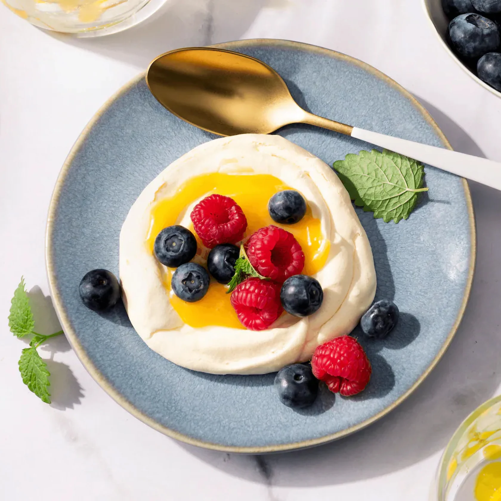 Blauer Keramikteller mit Joghurt, Honig, frischen Beeren und Minzblättern