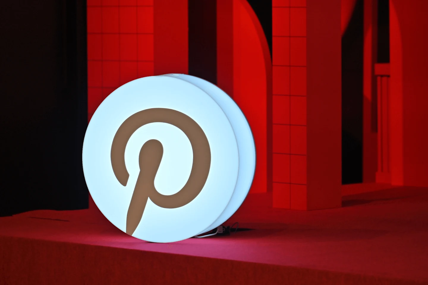 Large illuminated Pinterest “P” logo sign on a red stage, with red geometric set pieces in the background.