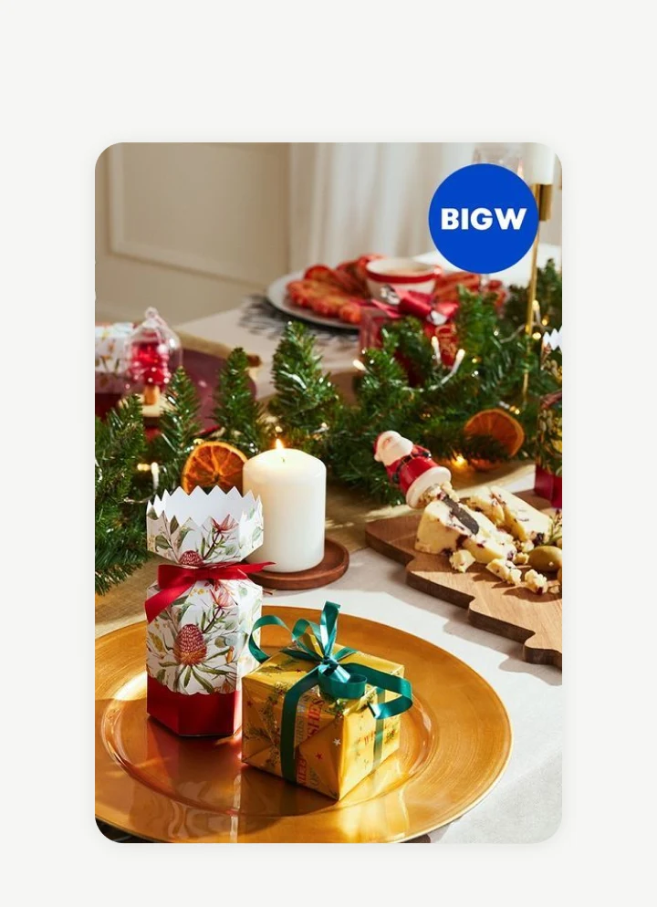 A dining table decorated for Christmas with gifts, a white candle, and festive food.