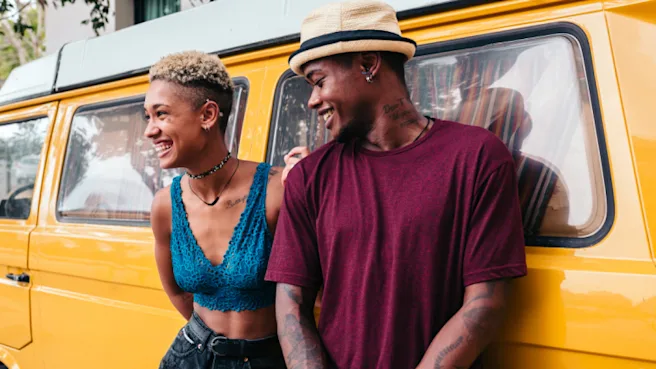 A Black woman and man leaning against the side of a yellow car