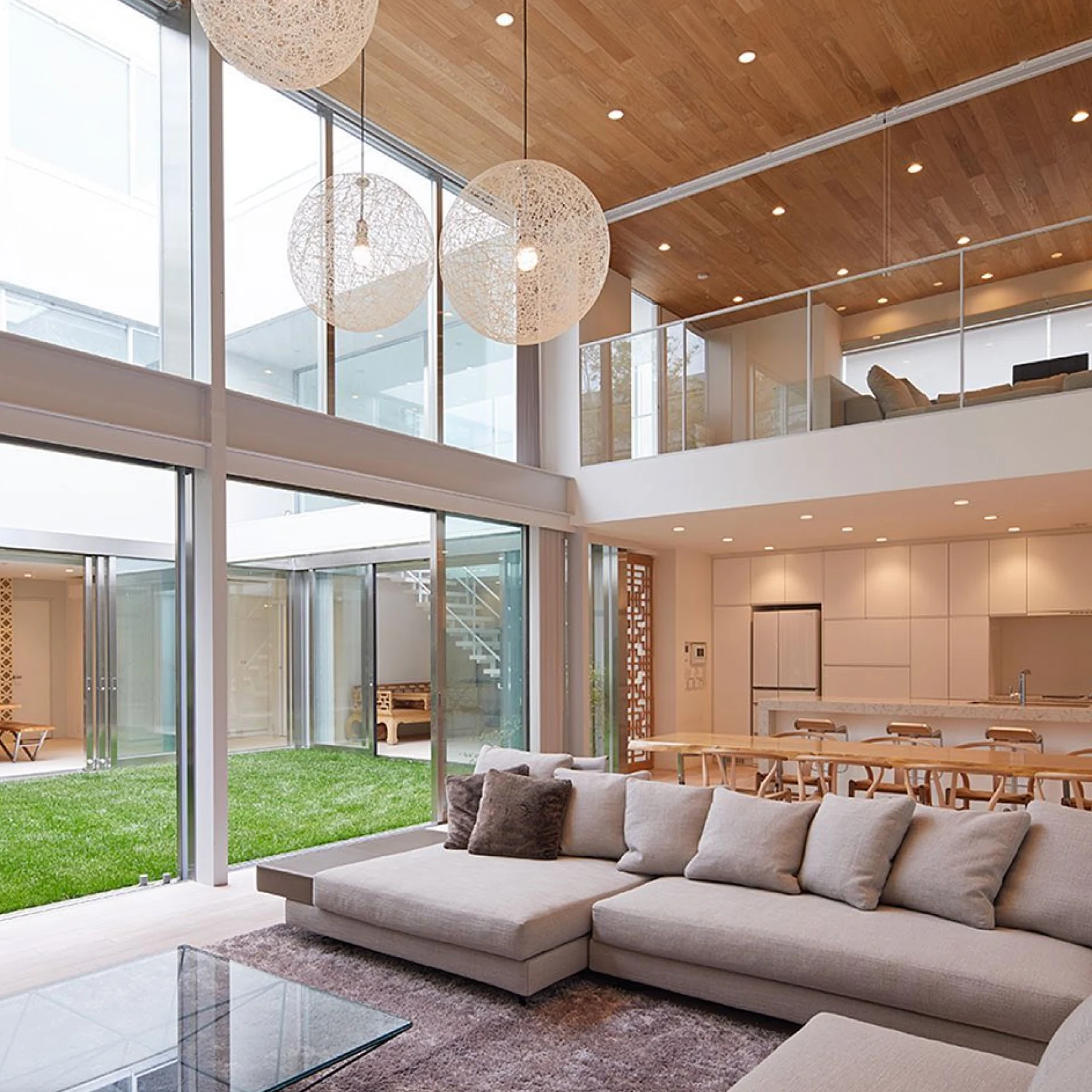 上部ロフト、長いダイニング ルーム テーブル、組み立て式ソファ、中庭に面した床までの長さの窓を備えた大きなオープン コンセプト ハウス