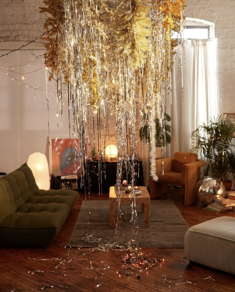 Stylish living room pictured with sparkly gold and silver centerpiece with tinsel and holiday lights hanging from ceiling