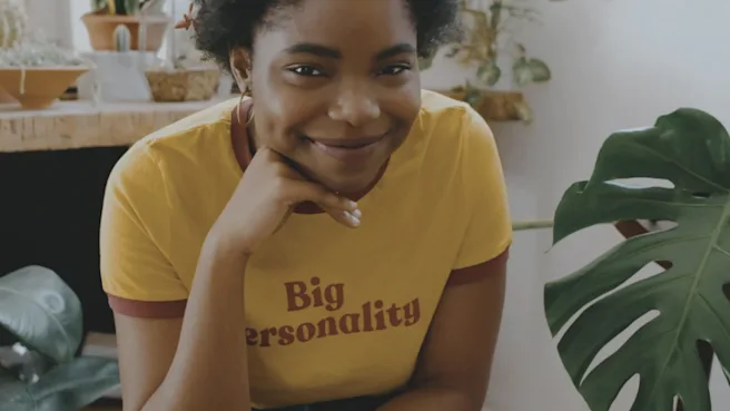 Black lady smiling wearing a yellow t-shirt with her chin leaning on her hand