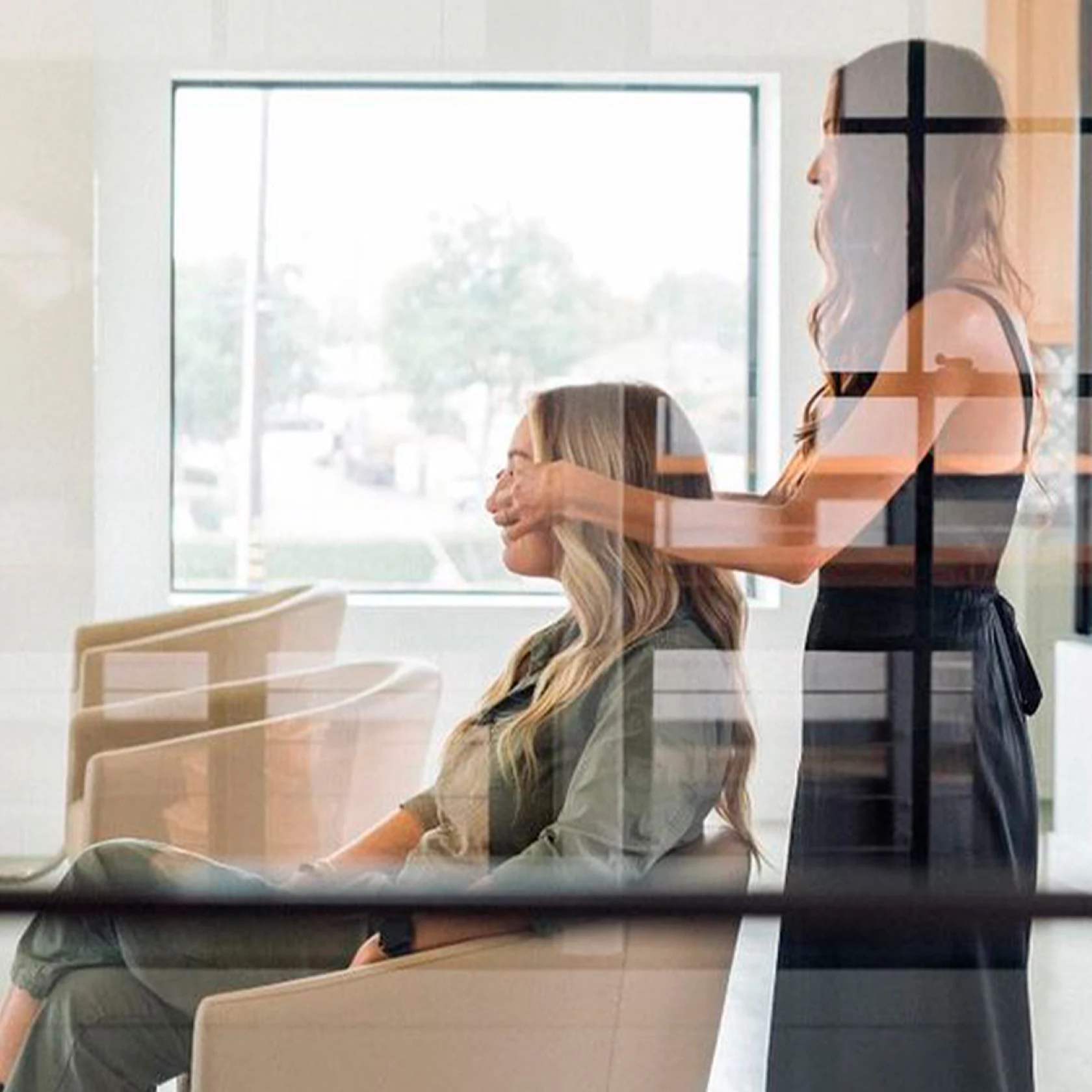 Foto a través de la ventana de una estilista de pie cubriendo los ojos de una clienta antes de revelar su cabello peinado