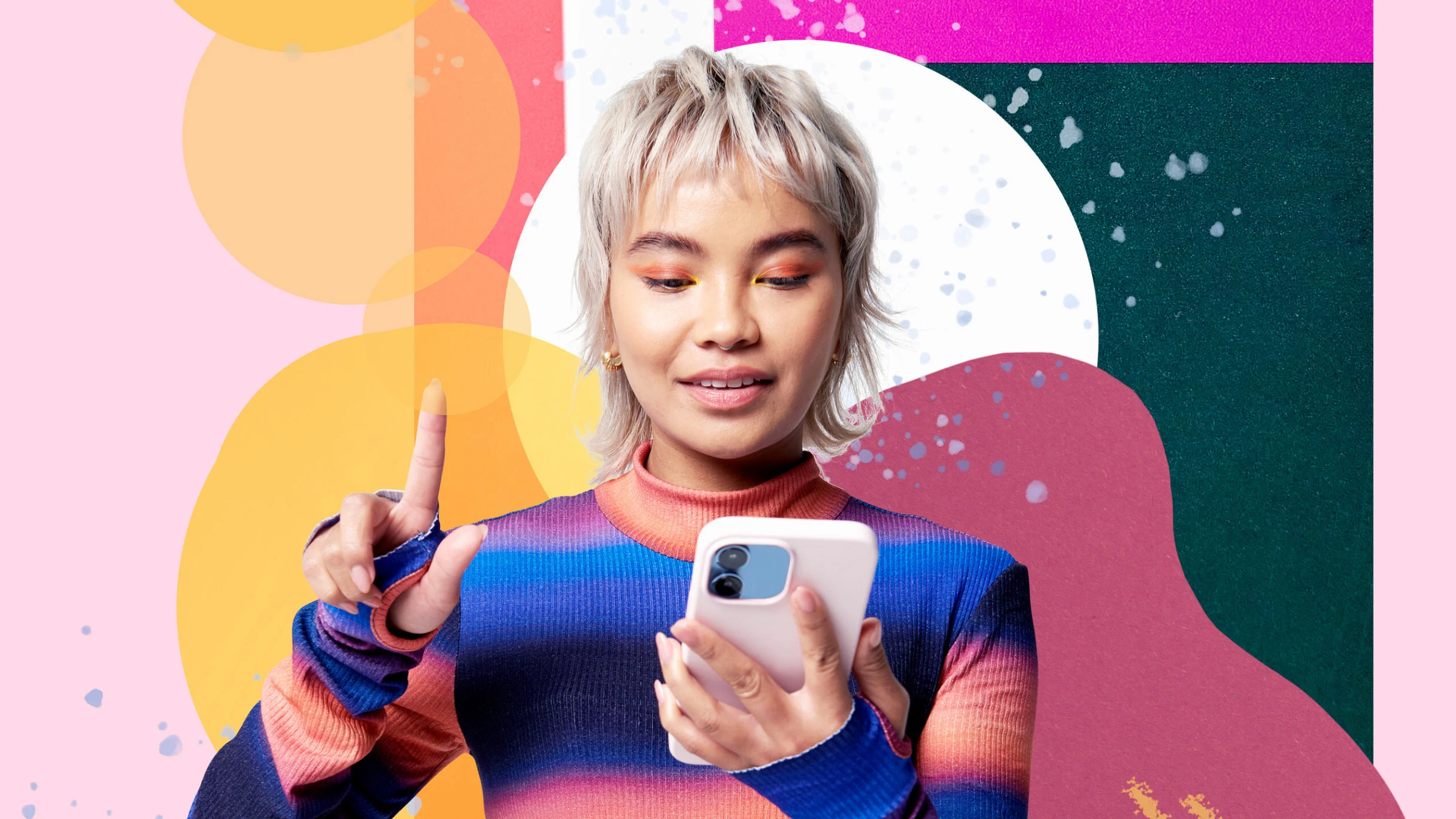 A woman with short blond hair in a bright striped top, is holding and looking at her phone in one hand and pointing upwards with her other hand on a very colourful and abstract background.