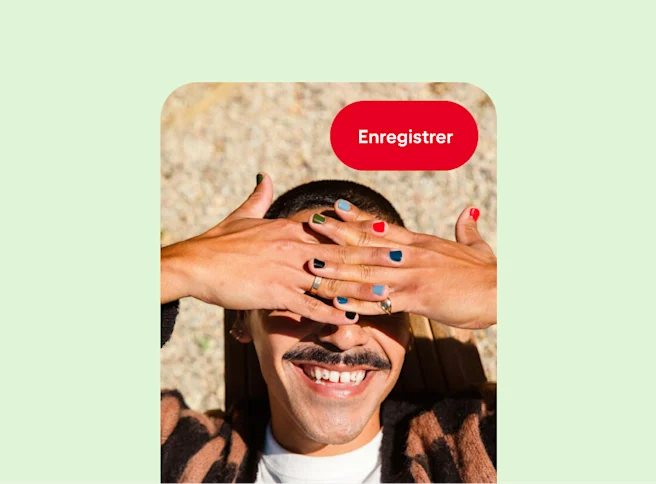 Une personne blanche sourit et se sert de ses mains pour se protéger les yeux du soleil. Chaque ongle est peint d’une couleur de vernis différente.