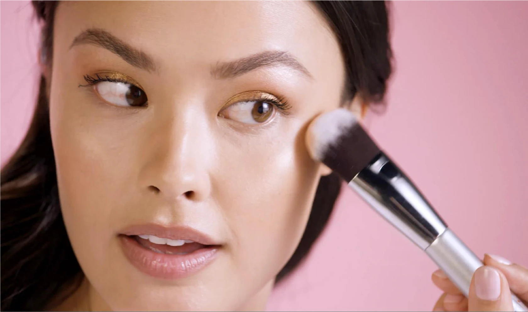 Picture of a woman applying makeup to her upper cheekbone.