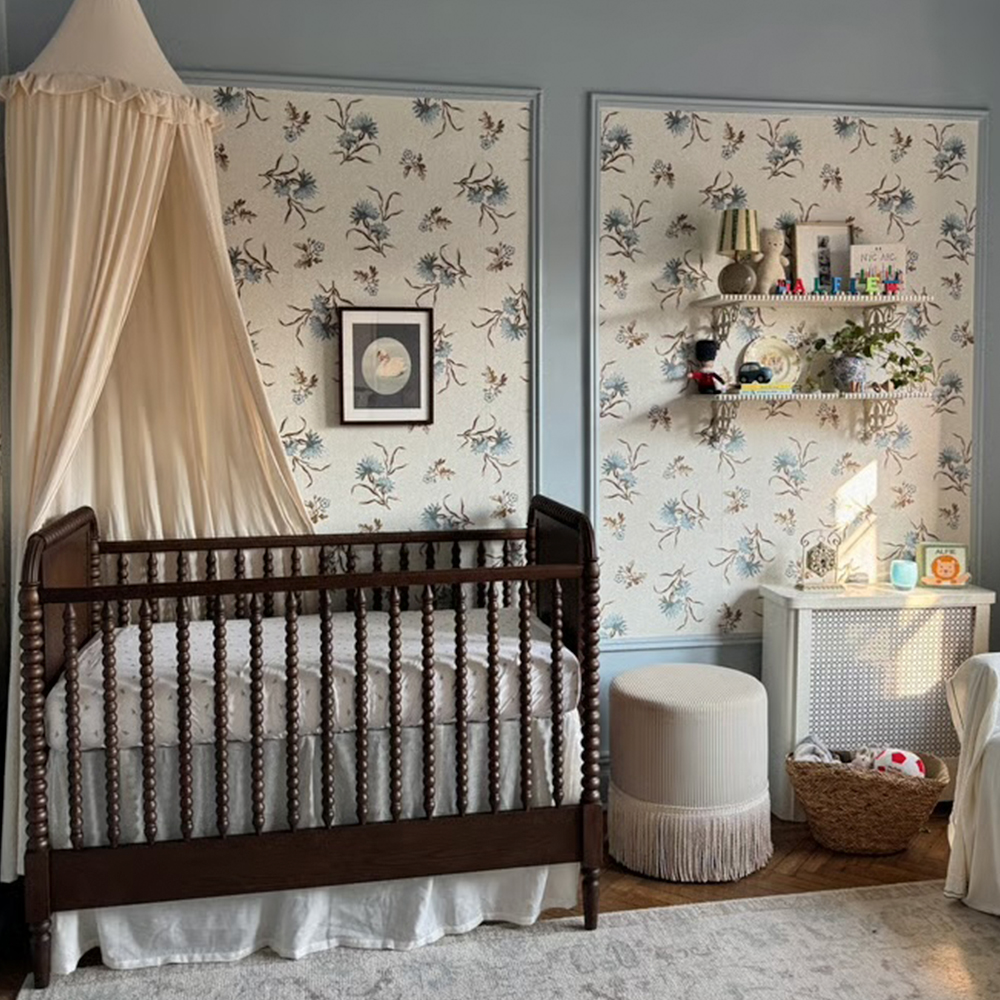 Nursery with tan and blue floral toss wallpaper and a canopy over the crib.