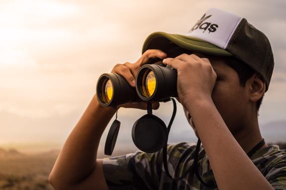 Man looking through binoculars at sunset.