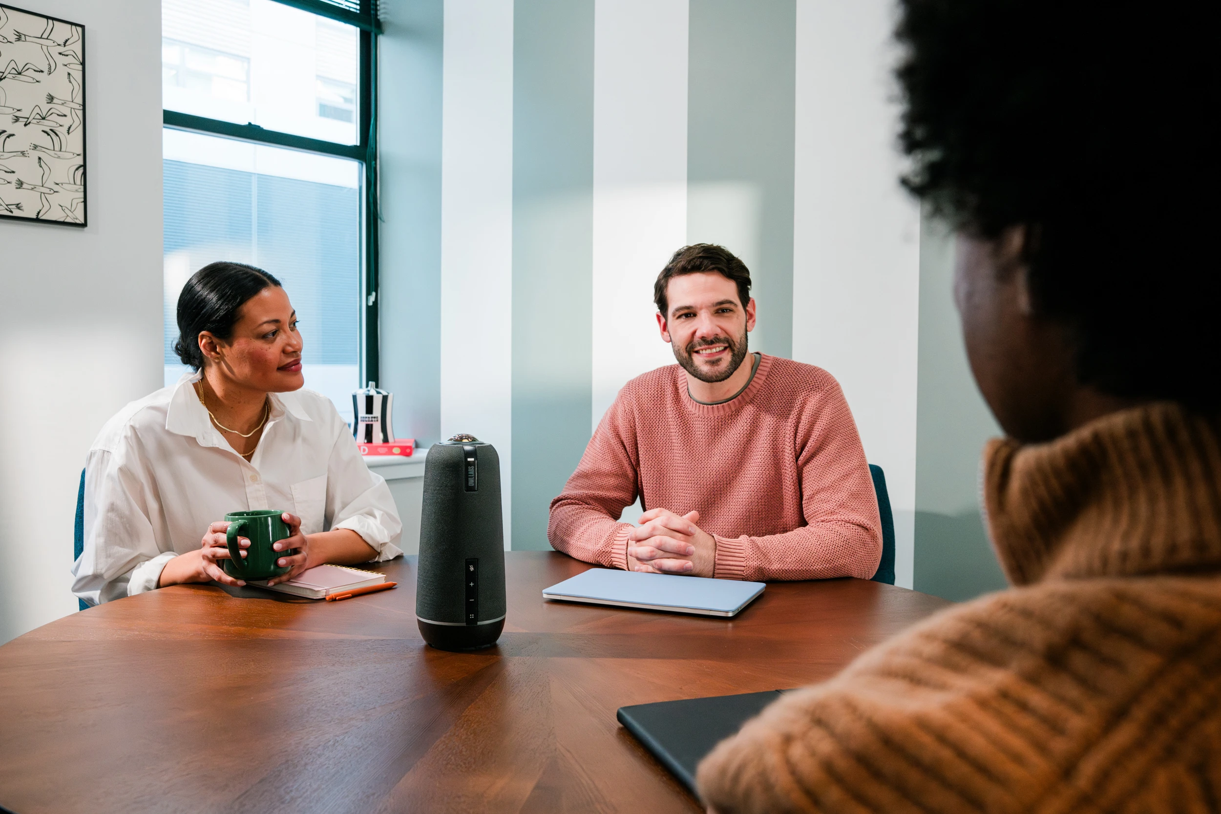 Colleagues engaging in a hybrid meeting using the Meeting Owl 4+ video conferencing device.