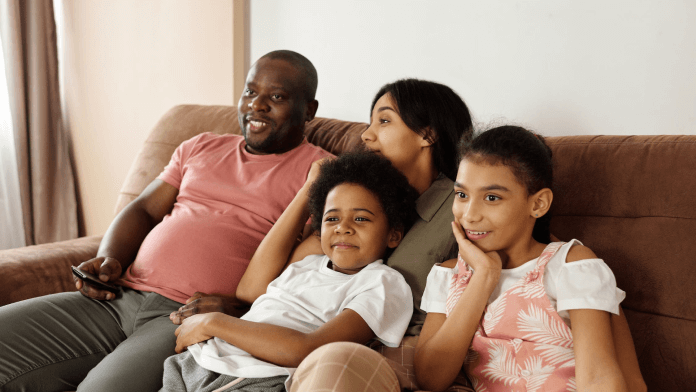 Family of 4 watching television together on a couch.