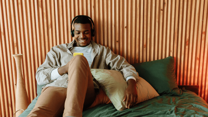 Young man using mobile smart phone while smiling and listening to headphones