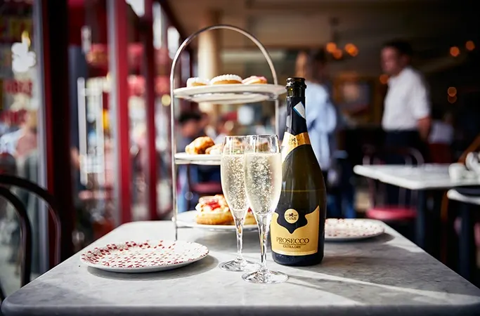 A cake stand filled with treats next to a bottle of prosecco A cake stand filled with treats next to a bottle of prosecco