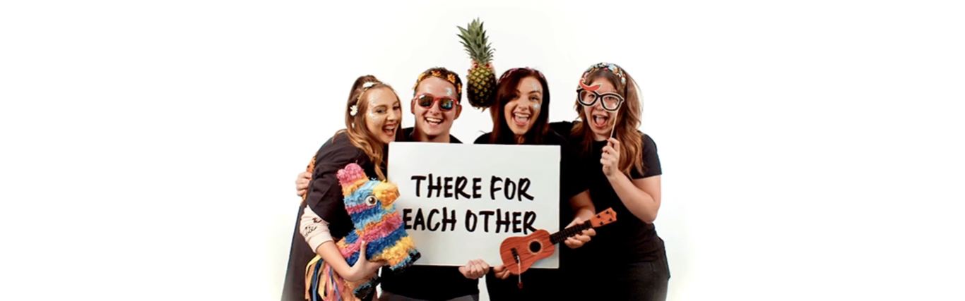 Smiling team members holding a sign that reads 'There for each other' Smiling team members holding a sign that reads 'There for each other'