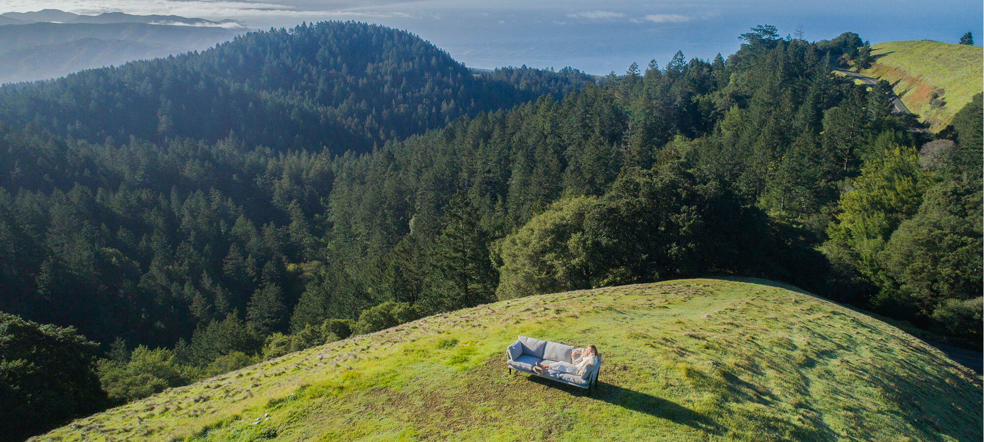 A photo of a women on Floyd sofa atop a green hillside.