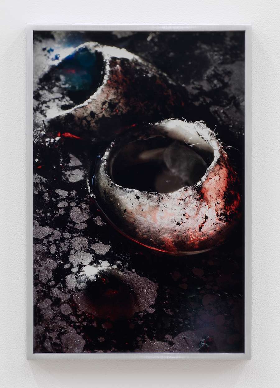 Two white circular objects are embedded into a ground, splattered with black and silver paint, appear to be like barnacles or craters on a moon.