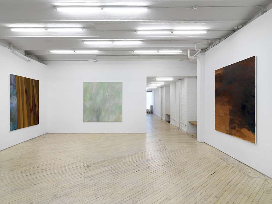 Three large, square abstract paintings installed on separate walls in a large gallery space with the long hallway in the back.