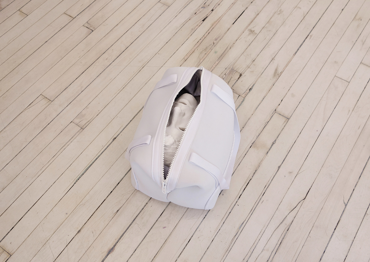image of a white gym bag on the floor with a white 3D printed male head peeking out from the zipper