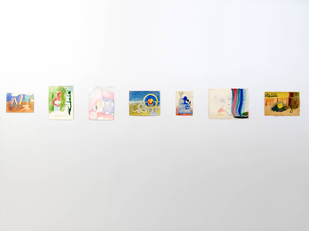 In a gallery space, a series of small works on paper are installed close together on a white wall. The drawings depict abstracted, cartoon-like character scenes in various patterns or open public spaces.