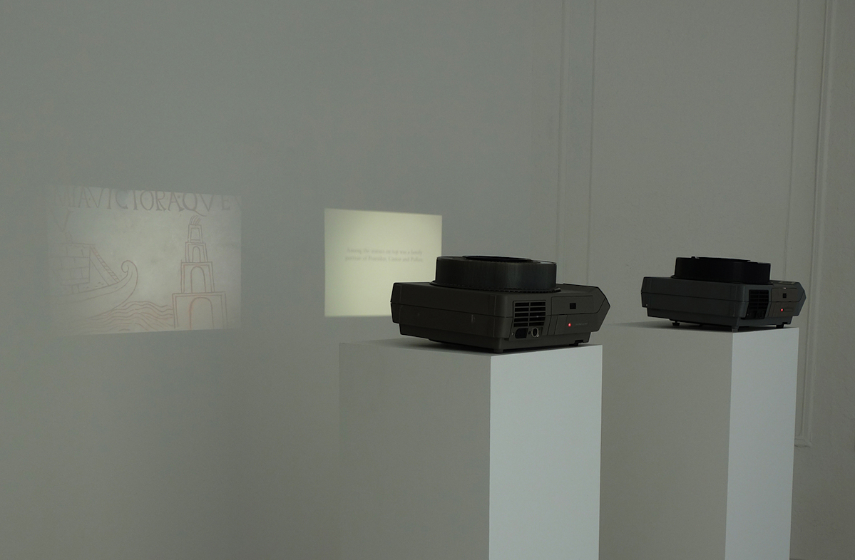 Two slide projectors on white plinths, projecting images of archival architectural images of the Pharos Lighthouse of Alexandria.