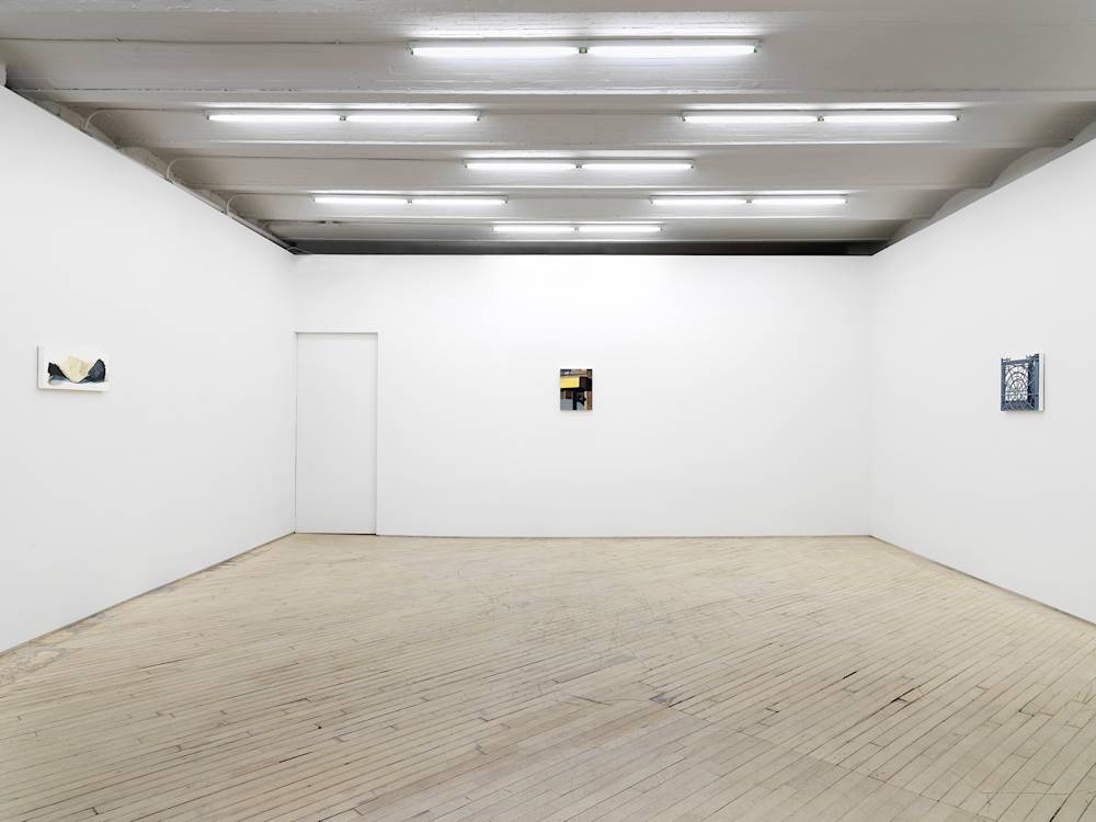 View of the gallery with white walls, fluorescent lights and light wood floors. Three very small paintings hang on the 3 visible walls. At left is a spare black and white thin horizontal composition. At center a vertical color painting showing a yellow awning on a city street and at right a grey and white square painting of a grey milk crate.
