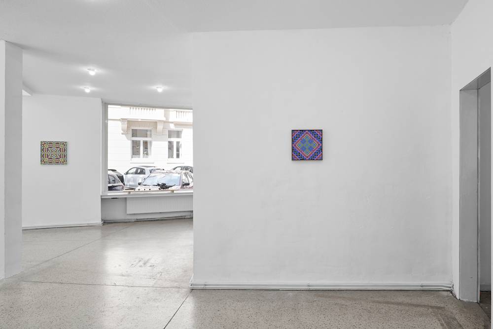 Image of a gallery space with a wall on the right, with a painting installed. To the left, there is a father wall with another painting installed. There is a window in the background as well.