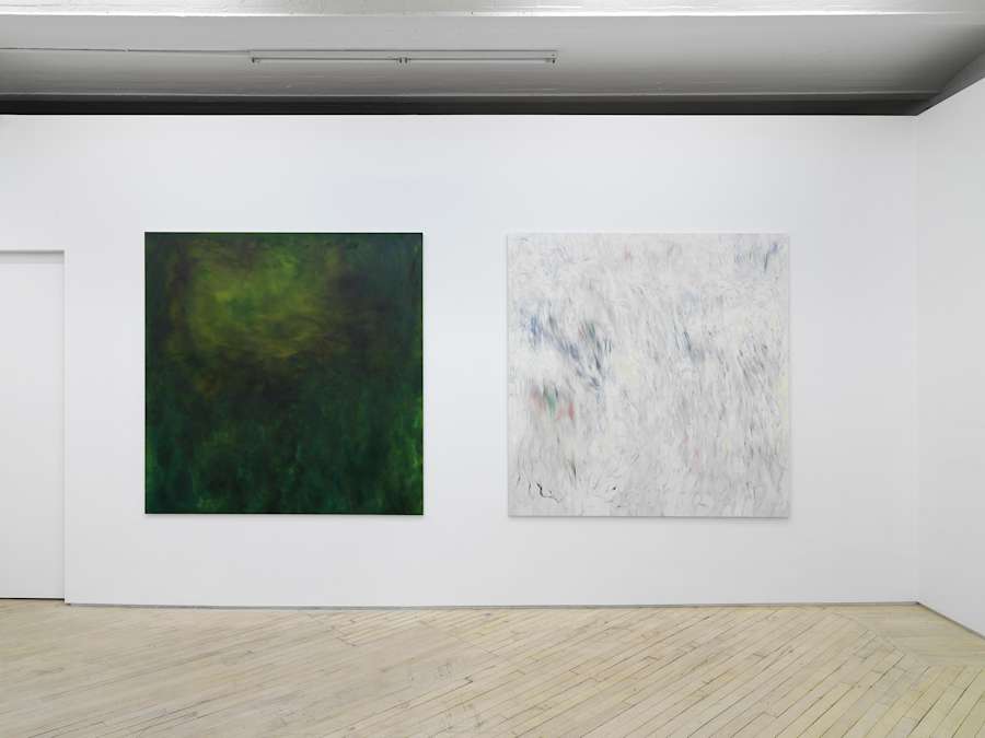 Two large square abstract paintings hung close together on a long gallery wall with a closed door way to the left.