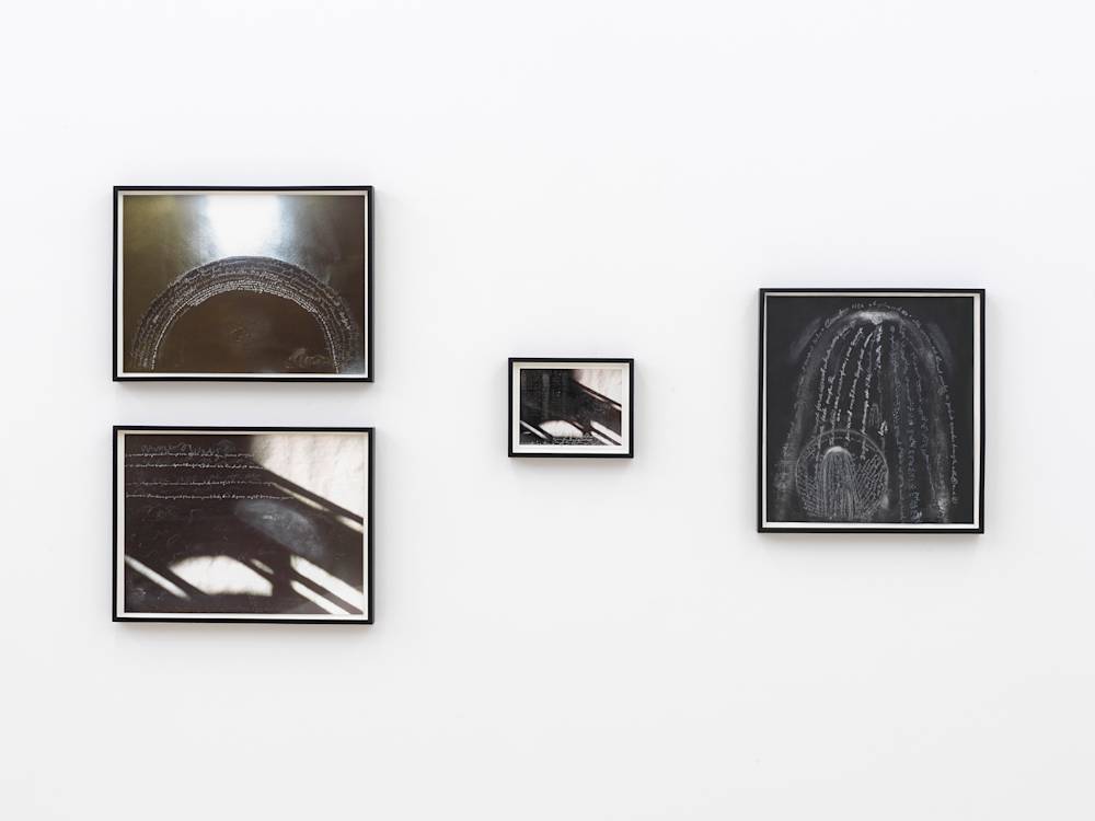 A salon style handing of four black and white artworks resembling photographs or drawings with handwritten chalk notes at the surface. The frames are black.