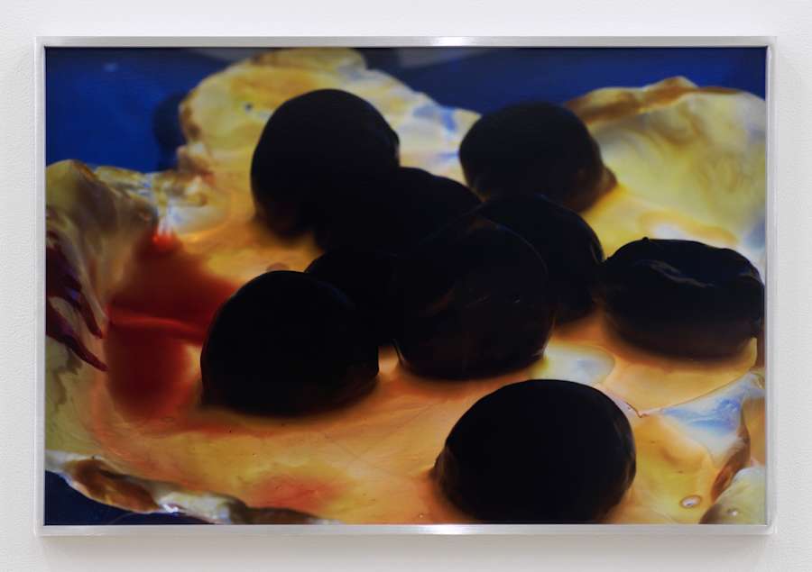 A group of water chestnuts, mostly in shadow and almost completely black, sit on a flat torn object that is covered in a sticky looking orange liquid.