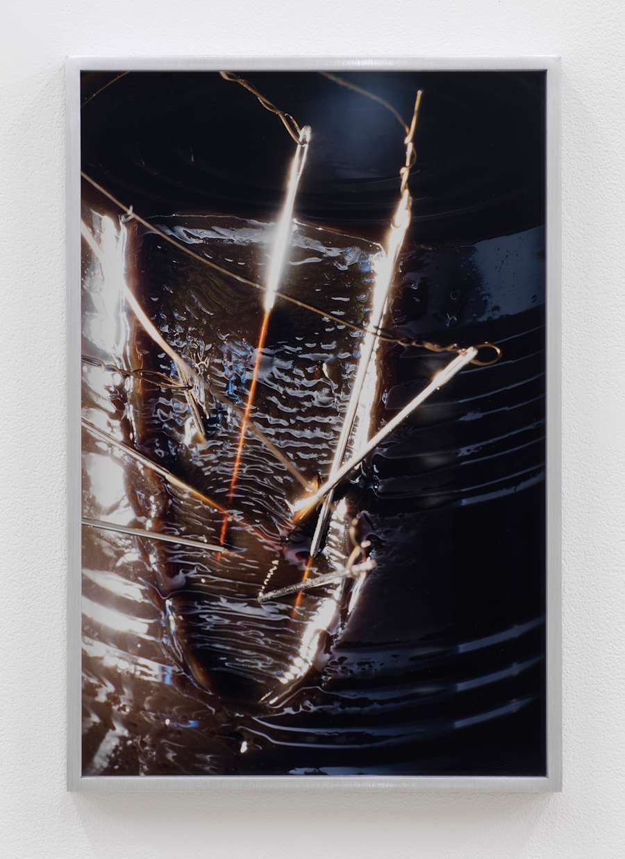Grass jelly recently emptied from a can, still with the circular can marks around its shape, has a slice taken out of it and is pierced with several sewing needles that glisten in the light.