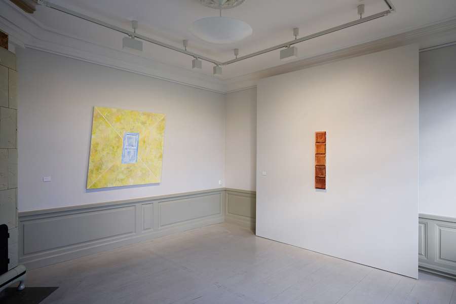 Installation view of the exhibition "Början och slut" at Fullersta Gård in Stockholm. On the left is a trapezoidal canvas with a door depicted against a yellow background, to the right is a small, skinny painting of a chocolate bar.