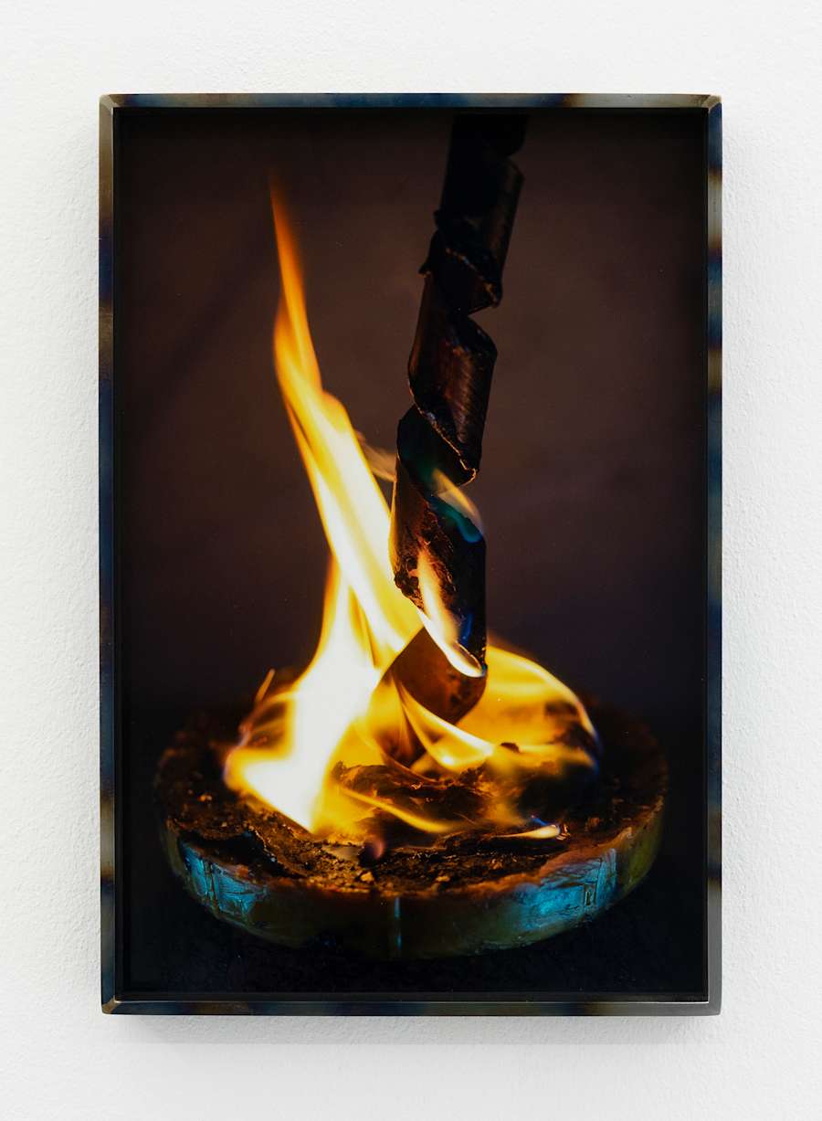 A circular disc contains some brown substance that is on fire, with a spiraled stick standing upwards out of the fire.