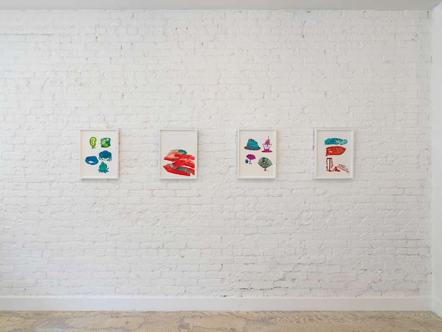 In a gallery space, four cartoon-like handmade drawings are hung in white frames evenly spaced apart. The most commanding colors are hues of greens, blues, reds, and purples.
