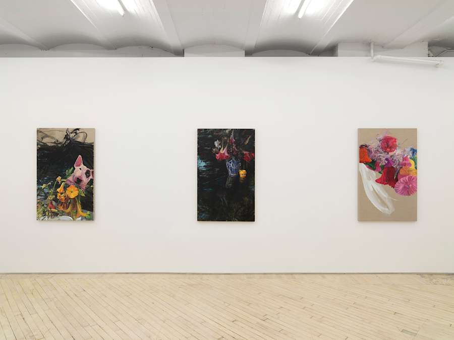 In a gallery space, three vertical paintings are hung evenly spaced apart. The painting contain gestural marks in bright colors next to representational forms such as an identifiable dog, flowers, and cups.