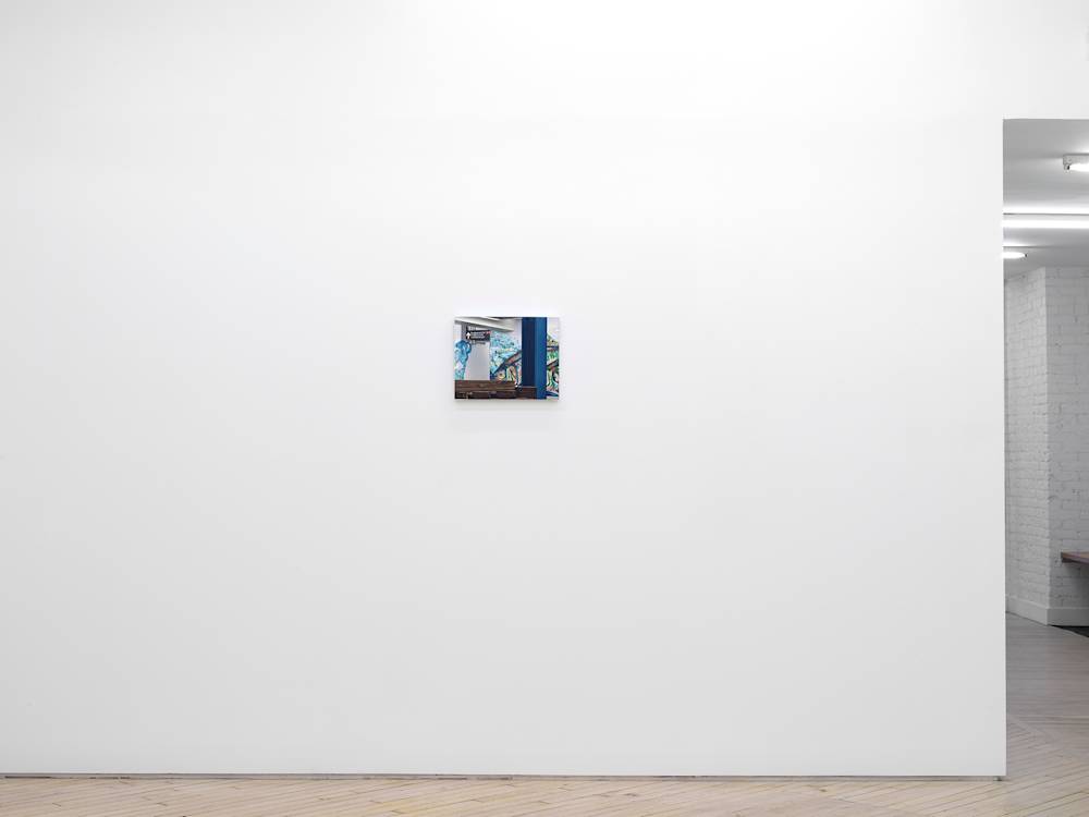 Installation view of a small painting on a white wall depicting the Delancey Essex subway station, with a wooden bench and blue metal pillar obscuring a mosaic tile mural of a colorful fish.